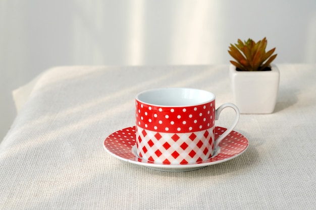 Tasse à café rouge et blanc et pot de petit arbre sur fond de nappe de tissu blanc