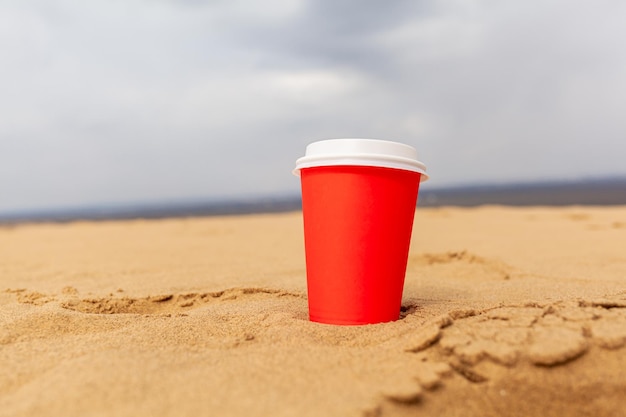 Une tasse de café rouge ou une boisson chaude recouverte d'un couvercle dans le sable du désert Bord de mer de sable