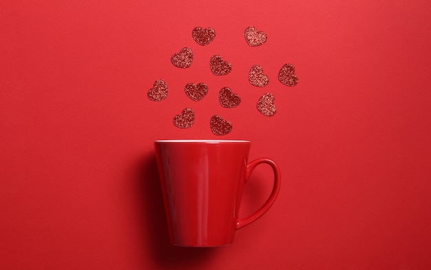 Tasse à café rouge avec des coeurs de paillettes rouges sur le mur rouge. Composition plate. Romantique, concept de la Saint-Valentin.