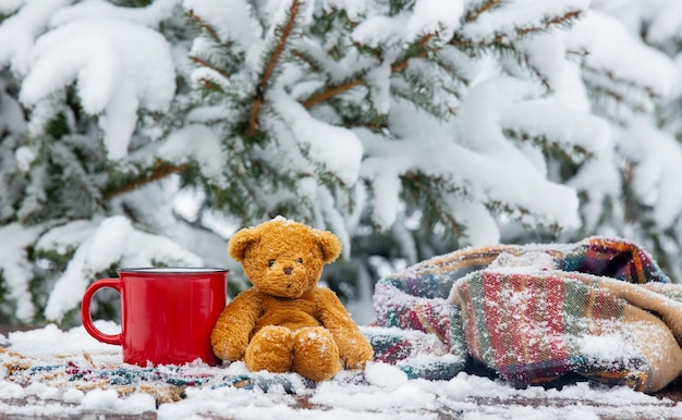 Tasse de café rouge et écharpe avec ours en peluche sur table en bois dans le blizzard