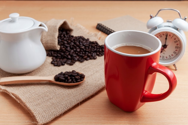 Tasse à café rouge avec grains de café et blanc réveil sur la table d&#39;affaires