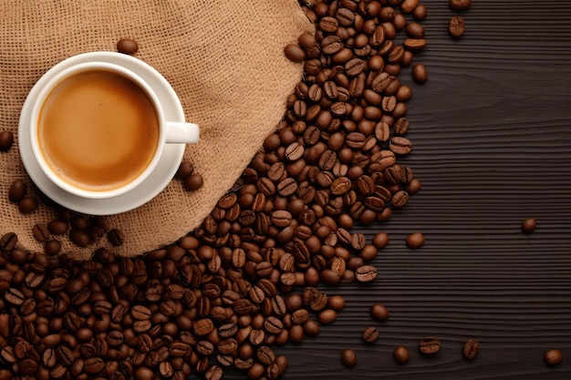 Une tasse de café sur un sac en drap et des grains de café sur fond en bois