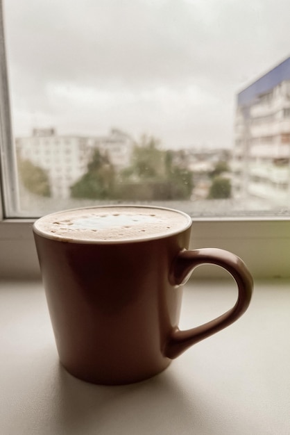 Une tasse de café se dresse sur le rebord de la fenêtre un jour de pluie nuageux