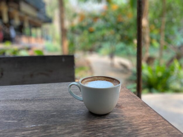 Une tasse de café se trouve sur une table à l'extérieur devant un jardin