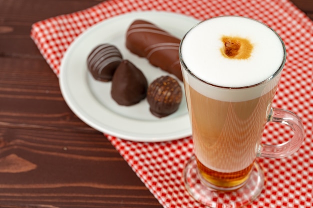 Tasse de café et soucoupe avec des bonbons au chocolat sur la table en bois se bouchent