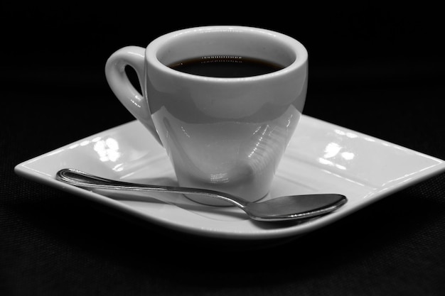 Tasse de café sur soucoupe et cuillère sur fond noir.
