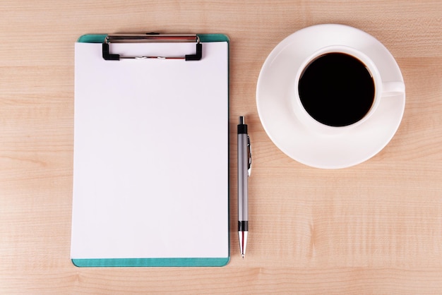 Tasse de café sur soucoupe avec feuille de papier et stylo sur fond de table en bois