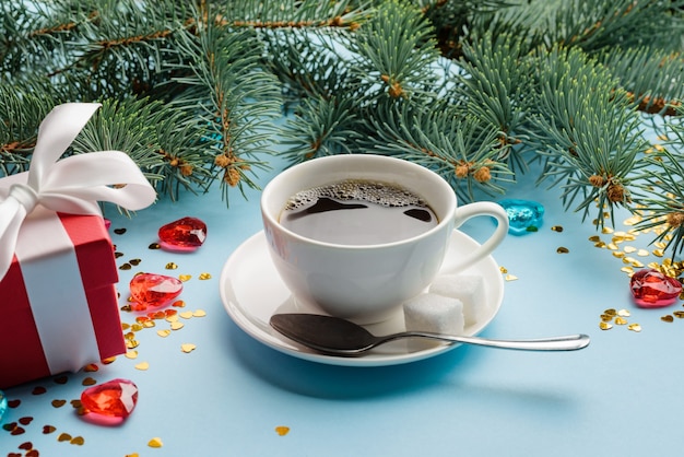 Une tasse de café sur une soucoupe parmi les décorations de Noël, les branches de sapin et les coffrets cadeaux.