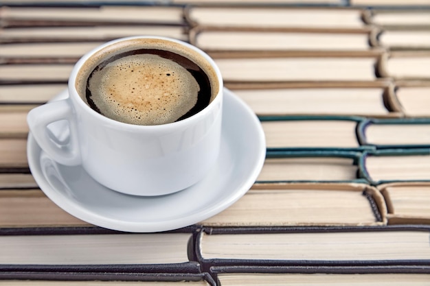 Une tasse de café sur une soucoupe et des piles de livres en papier