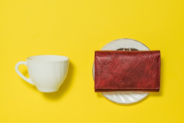 Une tasse de café, une soucoupe et un sac à main rouge sur fond jaune. Café et argent.