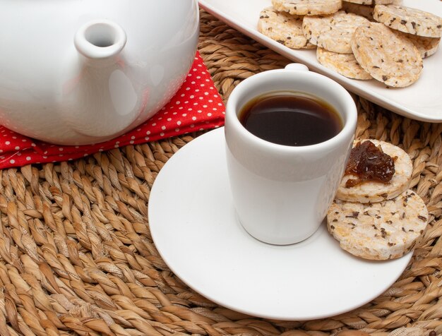 Une tasse de café sous la table de paille entourée d'un bol rempli de biscuits au riz et d'une cafetière