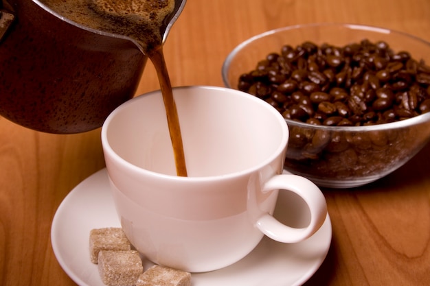 Tasse de café, sucre et haricots dans un bol en verre sur une table en bois