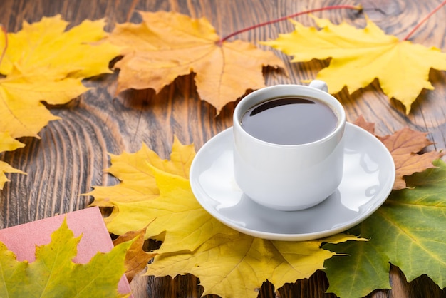 Tasse à café sur table en bois avec livre et feuilles d'érable automnales colorées