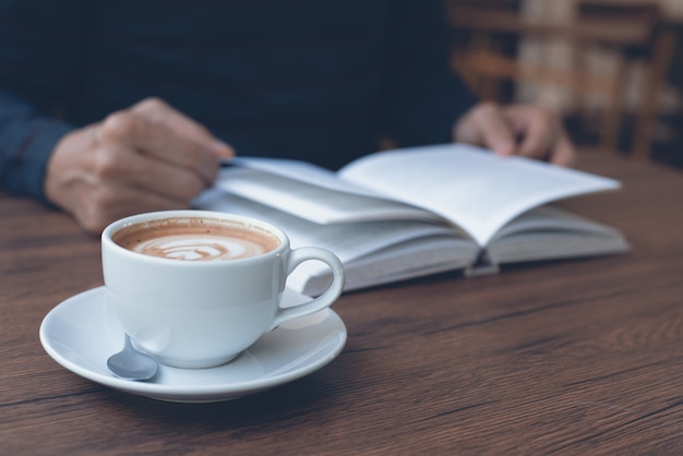 Tasse de café sur la table en bois avec un livre de lecture homme