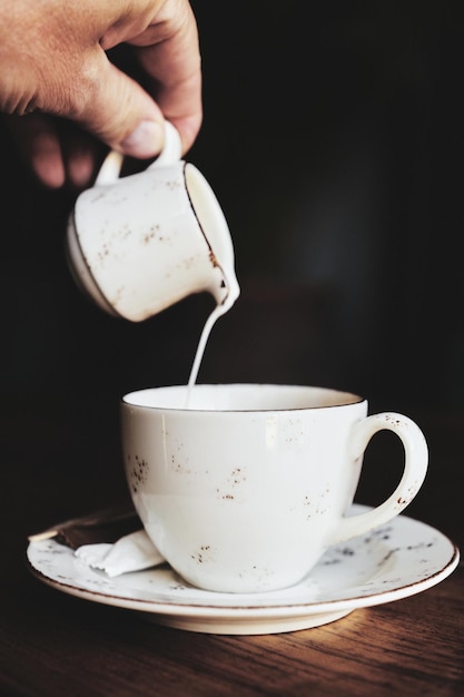 Tasse de café sur la table la main d'un homme verse du lait dans une tasse bruits de photographie couleur vintage et grain de film dans la photographie mise au point sélective du cadre vertical