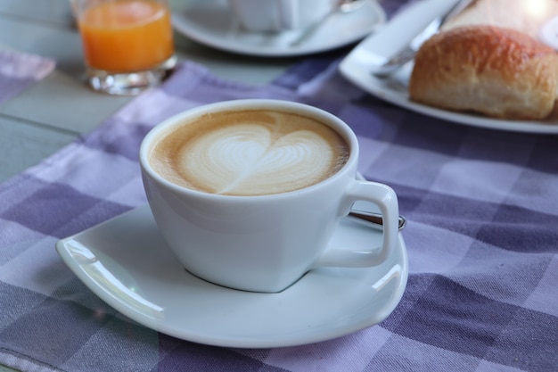 Une tasse de café sur la table avec une serviette, un cappuccino chaud avec de la mousse de lait cuit à la vapeur