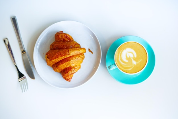 Une tasse de café tardif avec un design en forme de fleur sur le dessus et des croissants sur blanc