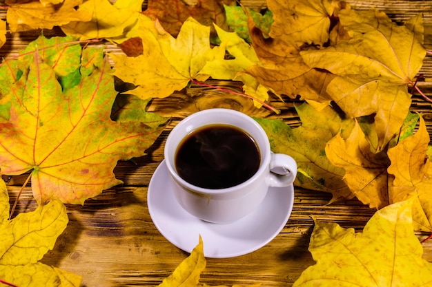 Tasse de café et tas de feuilles d'érable jaunes sur une table en bois