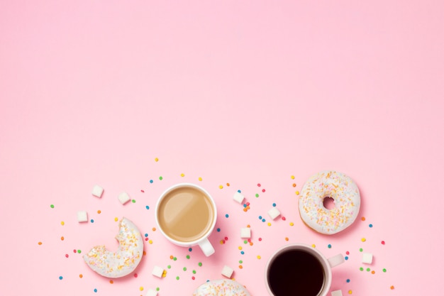 Tasse de café ou de thé, beignets sucrés savoureux frais, bonbons décoratifs colorés, morceaux de sucre sur fond rose.