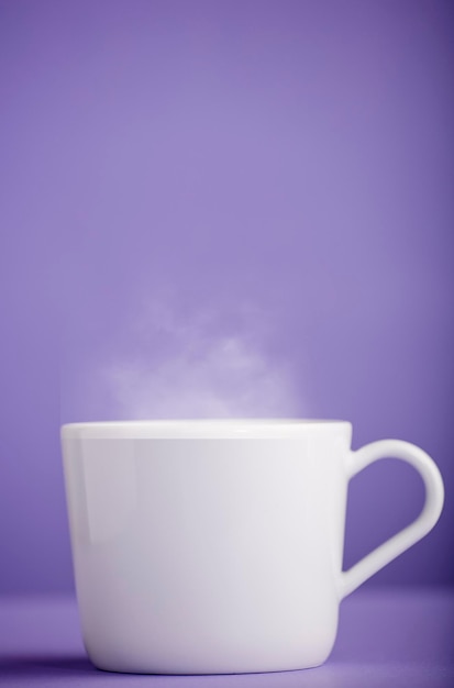 Tasse de café ou de thé en céramique blanche avec de la vapeur chaude avec un fond violet très peri