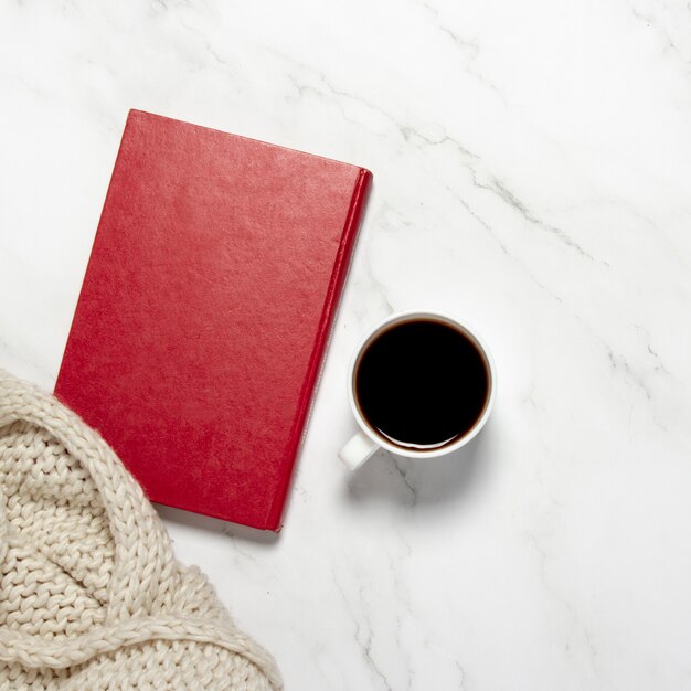 Tasse à café ou à thé, une écharpe tricotée et un livre sur une table en marbre. Concept de petit déjeuner, éducation, connaissances, lecture de livres, loisirs d'hiver. Mise à plat, vue de dessus