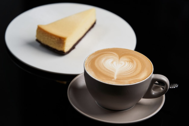 Tasse de café et tranche de gâteau au fromage sur une plaque blanche sur la table