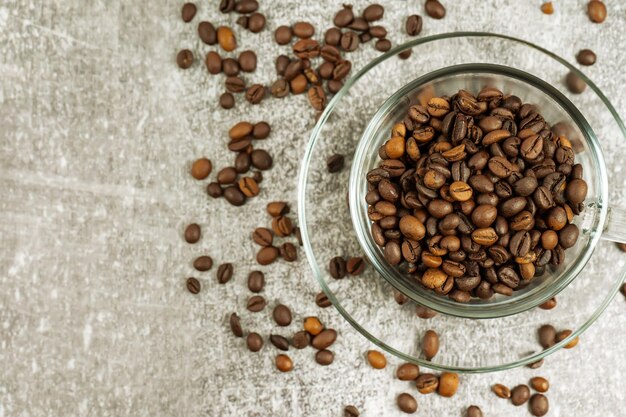 Tasse à café transparente avec grains de café torréfiés sur fond de béton gris avec espace de copie