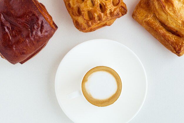 Une tasse de café et trois petits pains sur fond blanc. Style plat vue de dessus