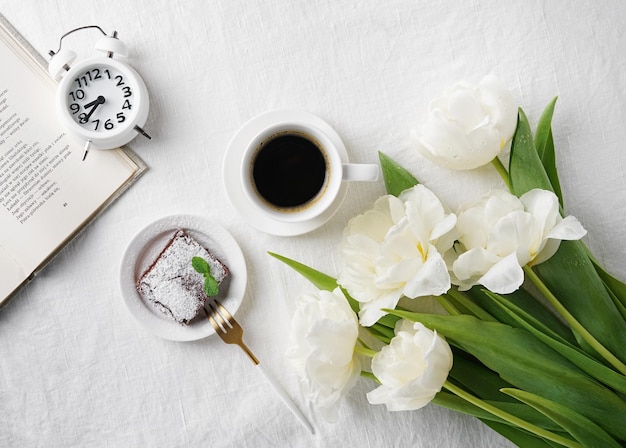 Tasse de café et tulipes blanches et alarme sur l'espace de copie vue de dessus de lit blanc