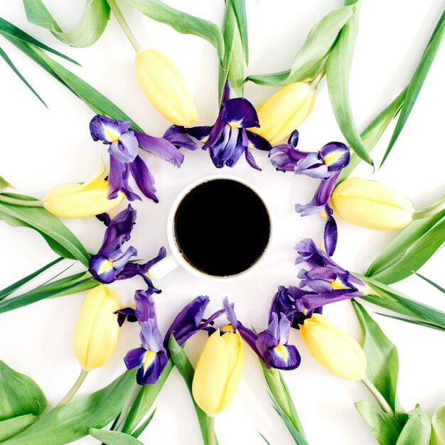 Photo tasse à café, tulipes jaunes et fleurs d'iris violets sur fond blanc. mise à plat, vue de dessus.