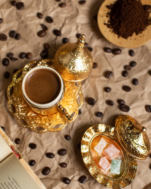 Une tasse de café turc avec un bord doré est posée sur une table avec des grains de café.