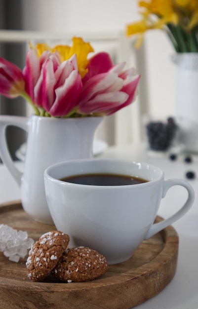 Une tasse de café et un vase avec des tulipes et des jonquilles sur un support en bois sur une table dans la cuisine