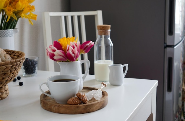 Une tasse de café et un vase avec des tulipes et des jonquilles sur un support en bois sur une table dans la cuisine