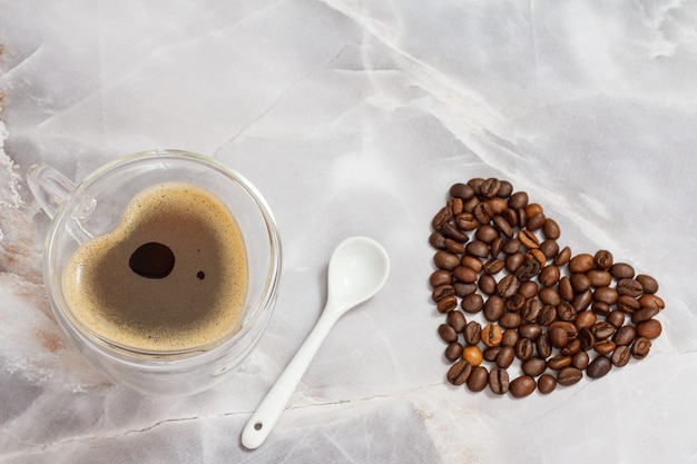 Tasse de café en verre, une cuillère et des grains de café torréfiés sur la table de la cuisine. Vue de dessus.