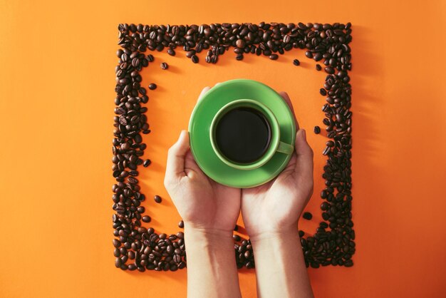 Tasse de café verte au milieu de grains de café en forme de carré sur fond orange