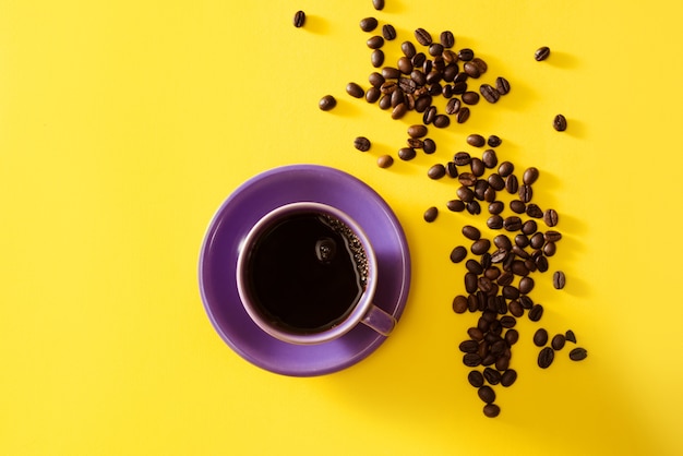 Tasse de café violet avec des grains de café sur fond jaune