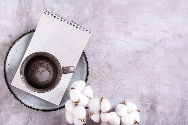 Tasse et cahier en céramique vides sur une assiette et une branche de coton sur une vue de dessus de fond gris