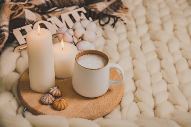 Tasse de cappuccino et biscuits, bougies, plaid à carreaux, inscription Accueil sur fond de couverture de fil épais. L'atmosphère de convivialité et de confort.