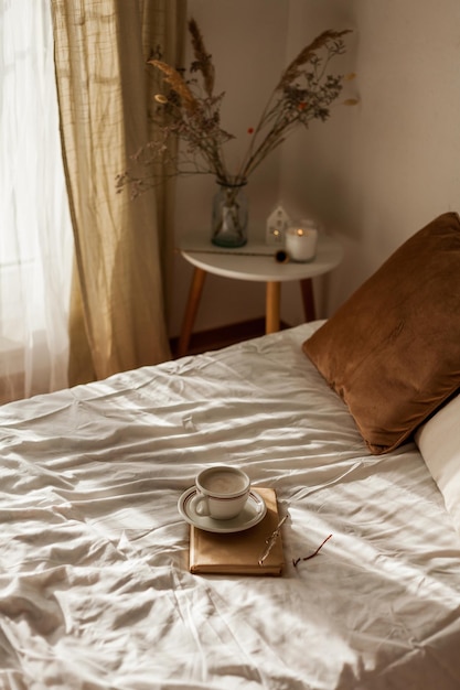 Une tasse de cappuccino chaud Un livre Des verres sur le lit Le petit déjeuner Une maison confortable Les détails du décor