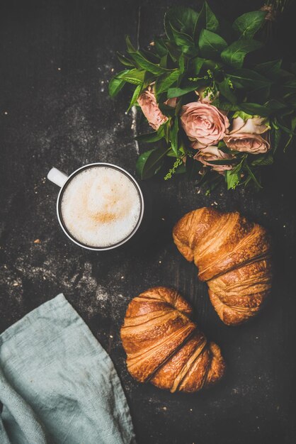 Tasse de cappuccino croissants frais et fleurs sur fond minable