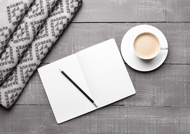 Tasse de cappuccino avec écharpe en laine grise et livre de journal sur la surface en bois