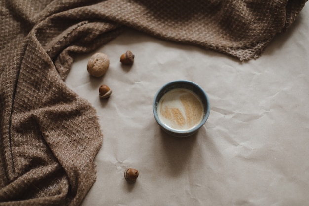 Tasse de cappuccino sur un fond de texture de papier brun avec des noix et des glands à carreaux chauds et confortables