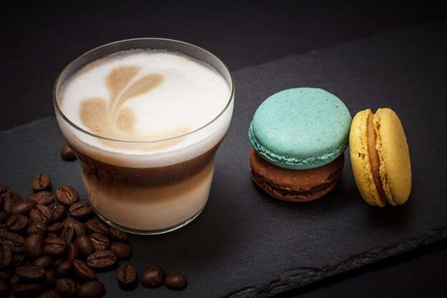 Tasse de cappuccino, grains de café et macarons sur fond noir. Vue de dessus.