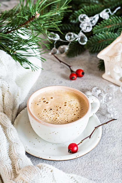 Une tasse de cappuccino (lat) sur fond clair près d'un arbre de Noël et de décorations.