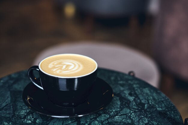 Une tasse de cappuccino avec de la mousse sur une table en marbre près de la fenêtre dans un petit café confortable.