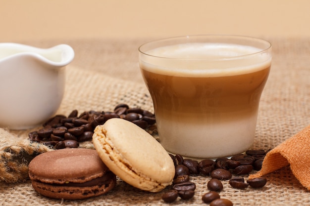 Tasse de cappuccino, saucière à la crème, grains de café et macarons sur fond de sac.