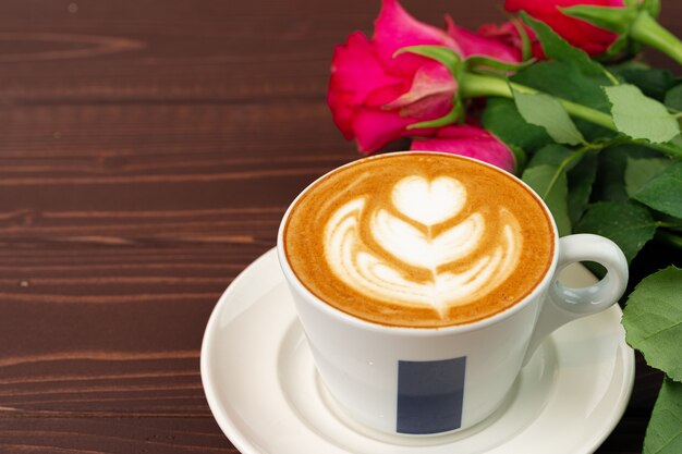 Tasse de cappucino avec art et bouquet de roses sur table en bois se bouchent