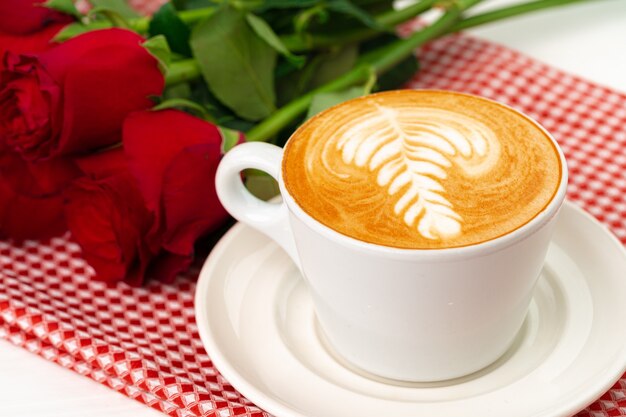 Tasse de cappucino avec art et bouquet de roses sur table en bois