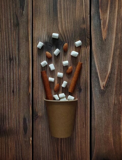 Tasse en carton pour café, amandes, guimauves, bâtons de cannelle sur fond en bois. Mise à plat.