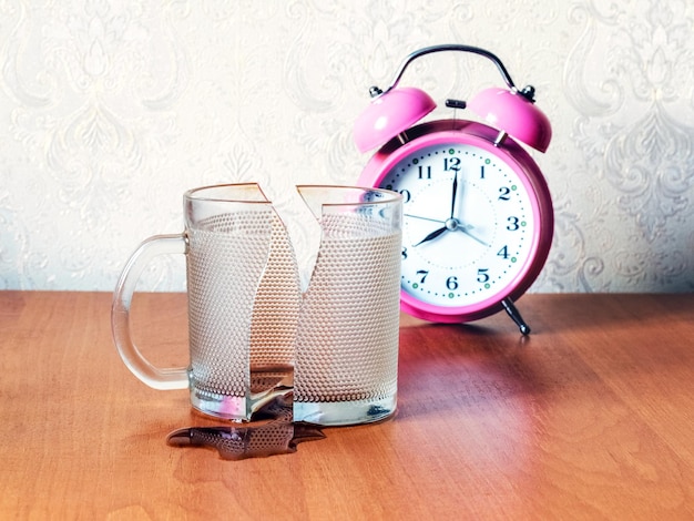 Tasse cassée avec du thé ou du café renversé sur la table du bureau près de l'horloge